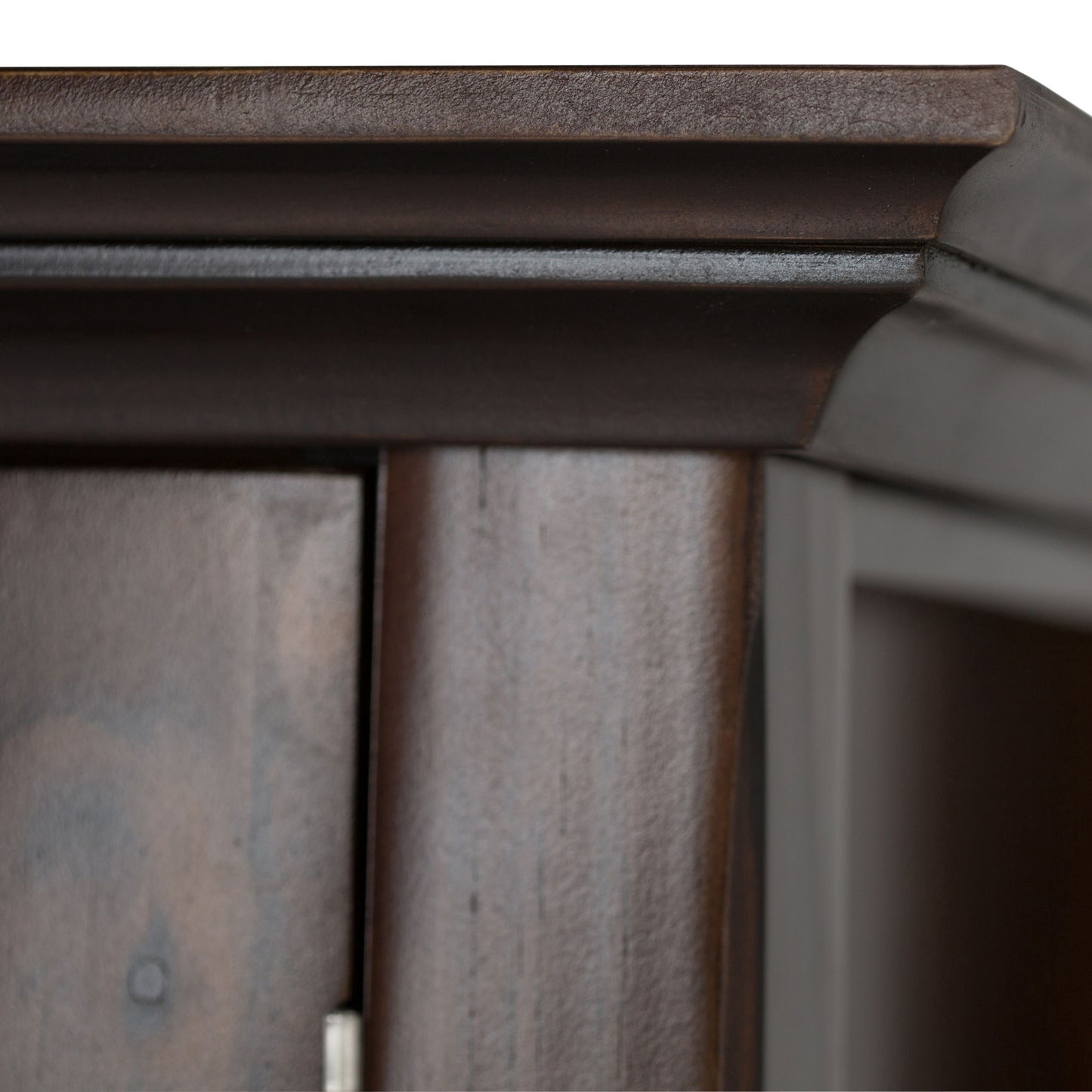 Close-up of the top corner of the Acadian Entryway Storage Cabinet in Brunette Brown, showcasing its smooth finish, raised decorative molding, and part of a door with visible hinge.