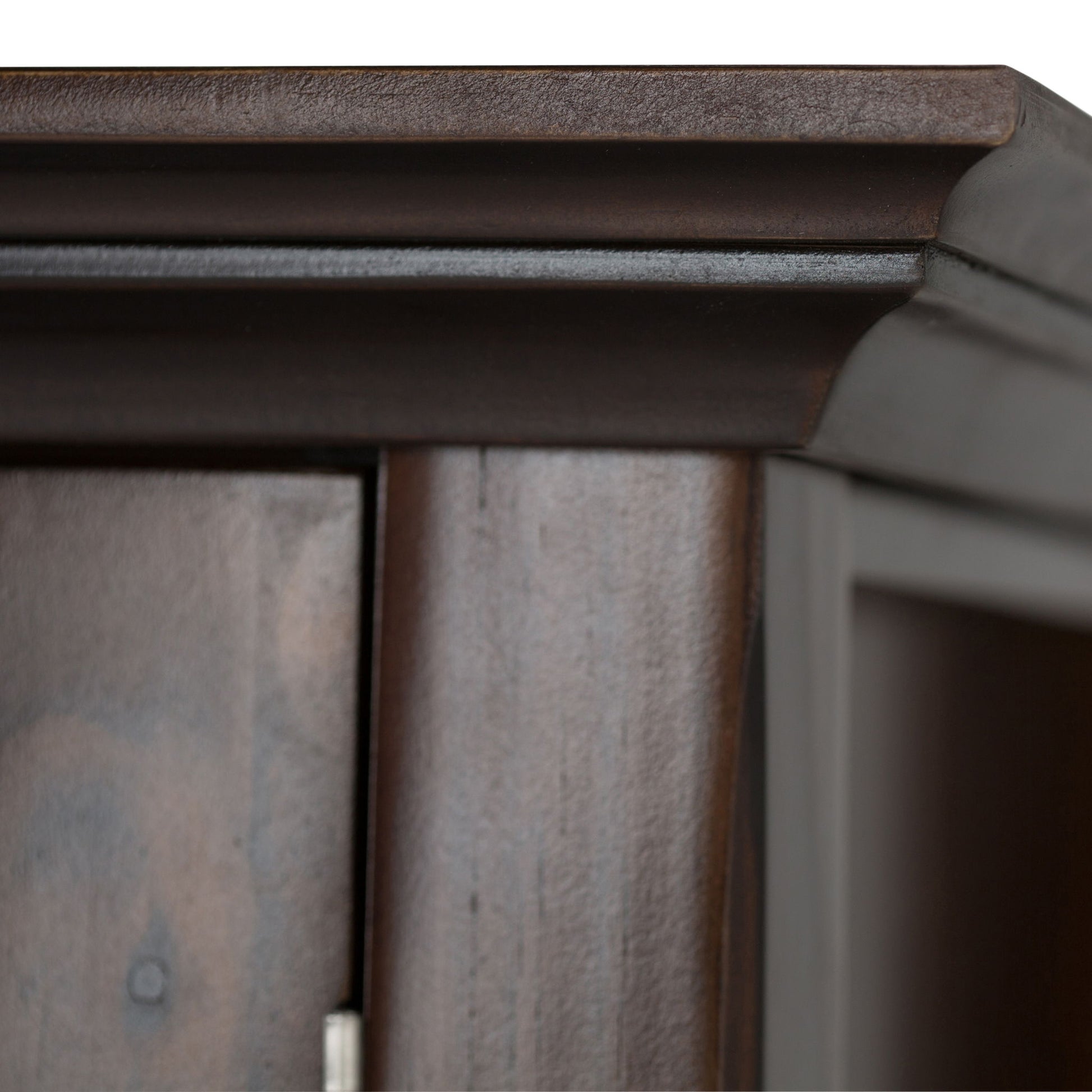 Close-up of the top corner of the Acadian Entryway Storage Cabinet in Brunette Brown, showcasing its smooth finish, raised decorative molding, and part of a door with visible hinge.