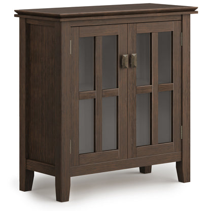 The Artisan - Handcrafted Low Storage Cabinet features dark wood, two glass-paneled doors with rectangular metal handles, four short legs, and a modern, simple design with vertical and horizontal wooden frames over the glass.