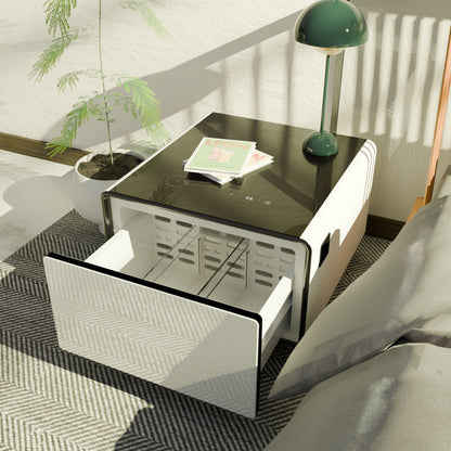 A Modern Smart Side Table with a glossy black top stands on a patterned rug by the bed, holding a green lamp and magazine. Its open drawer reveals storage, while built-in fridge, wireless charging, USB ports, and more add convenience.