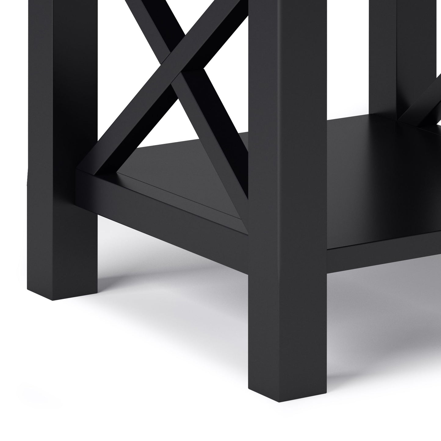 Close-up of the lower corner of the Kitchener - Handcrafted Table, a black wooden piece with crisscross supports and a bottom shelf, shown against a white background.