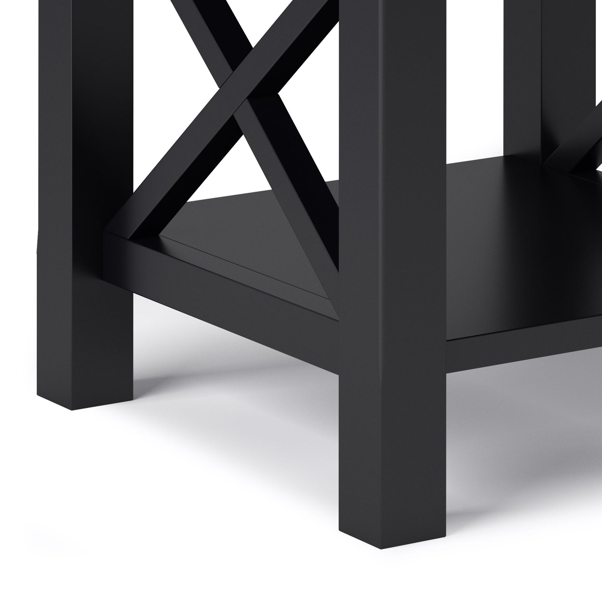 Close-up of the lower corner of the Kitchener - Handcrafted Table, a black wooden piece with crisscross supports and a bottom shelf, shown against a white background.