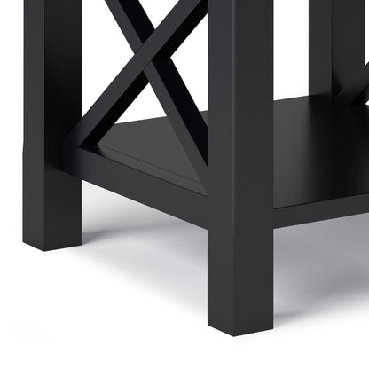 Close-up of the lower corner of the Kitchener - Handcrafted Table, a black wooden piece with crisscross supports and a bottom shelf, shown against a white background.