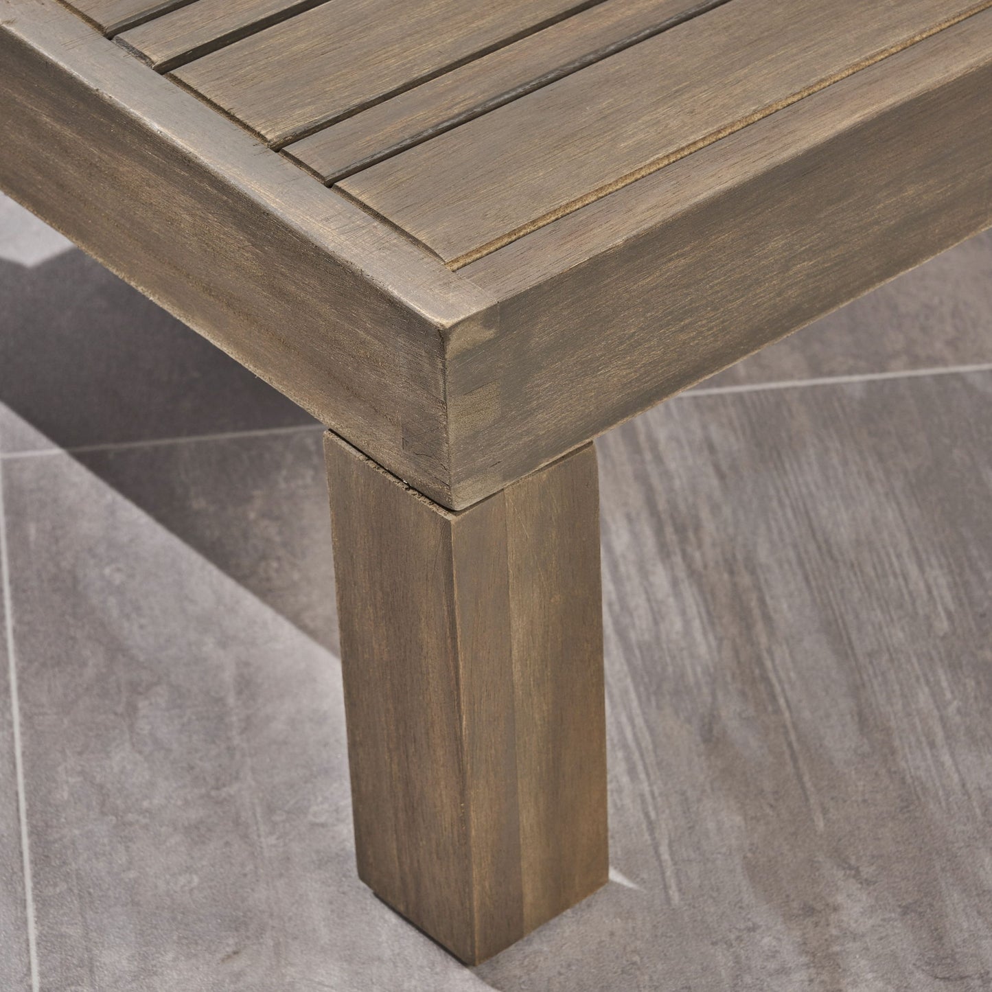 Close-up of the corner of the Alcove - L Shape Sofa Set, featuring a slatted wooden top and square legs, placed on a gray, stone-textured tiled floor.