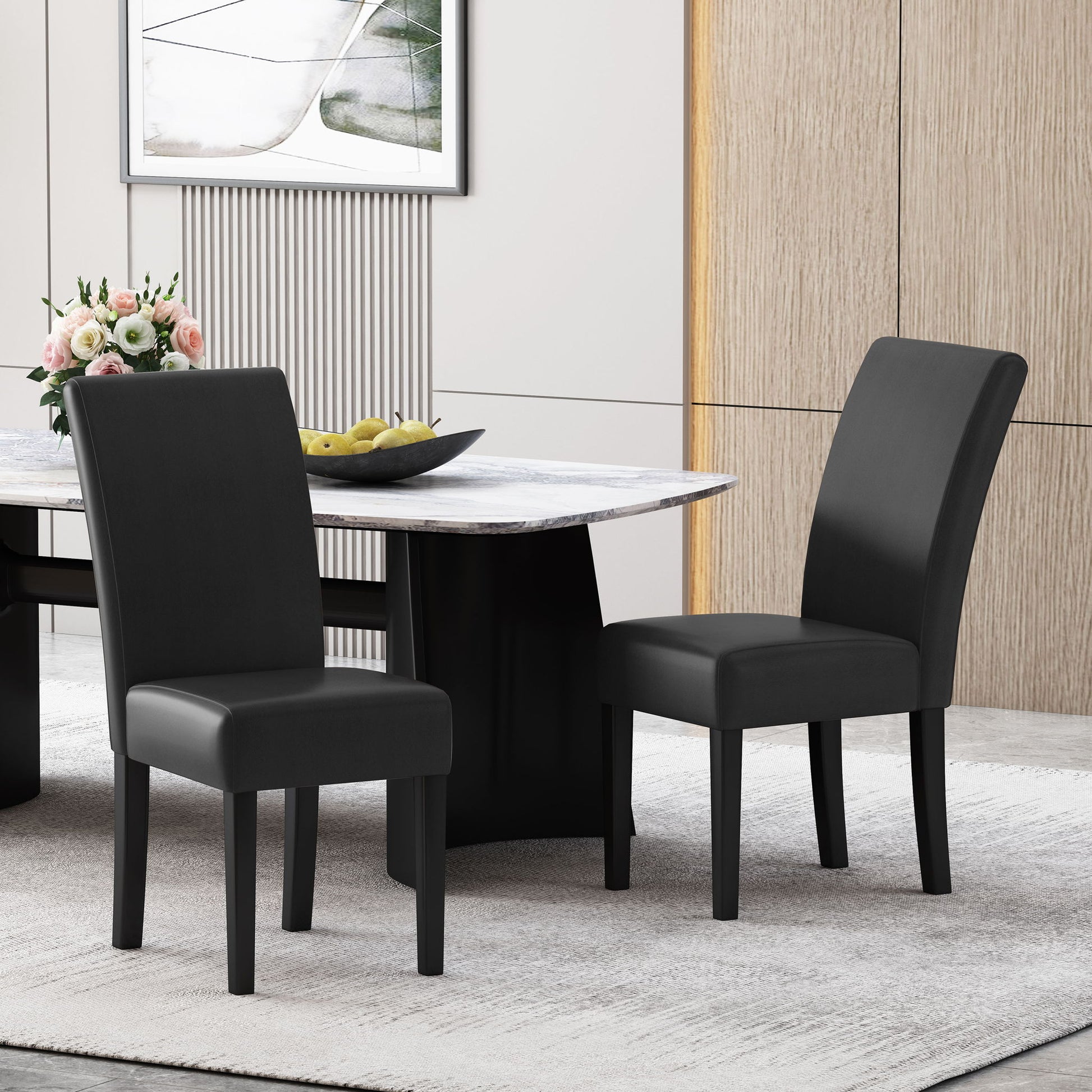 Two Contemporary Dining Chairs With Rubberwood Legs (Set of 2) in black are placed by a modern marble-top dining table. The stylish, minimal dining room features a bowl of green apples and a vase of flowers on the table.