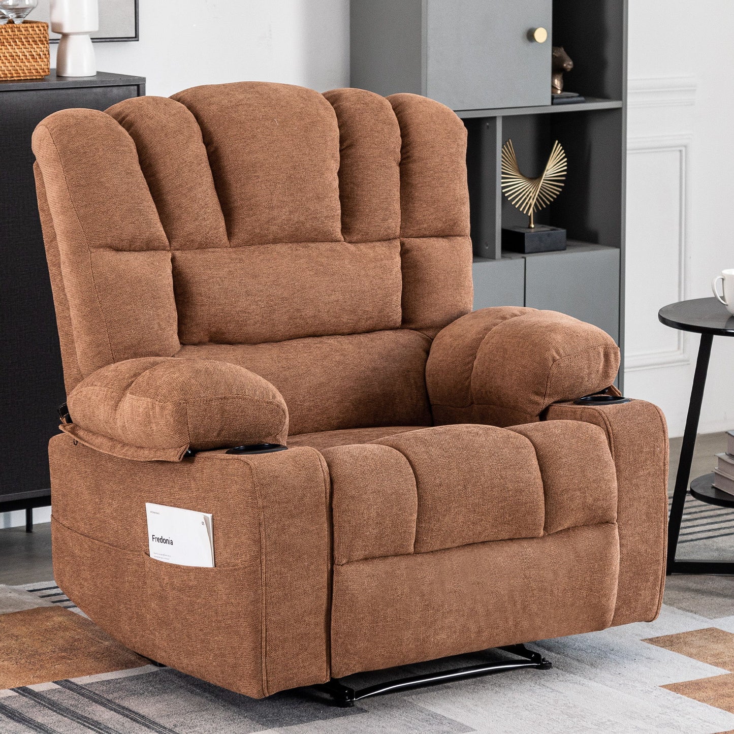 The Massage Recliner Chair Sofa With Heating Vibration, in plush brown with padded armrests and backrest, sits in a modern living room. A small white card is in its side pocket, and decorated shelves are visible in the background.