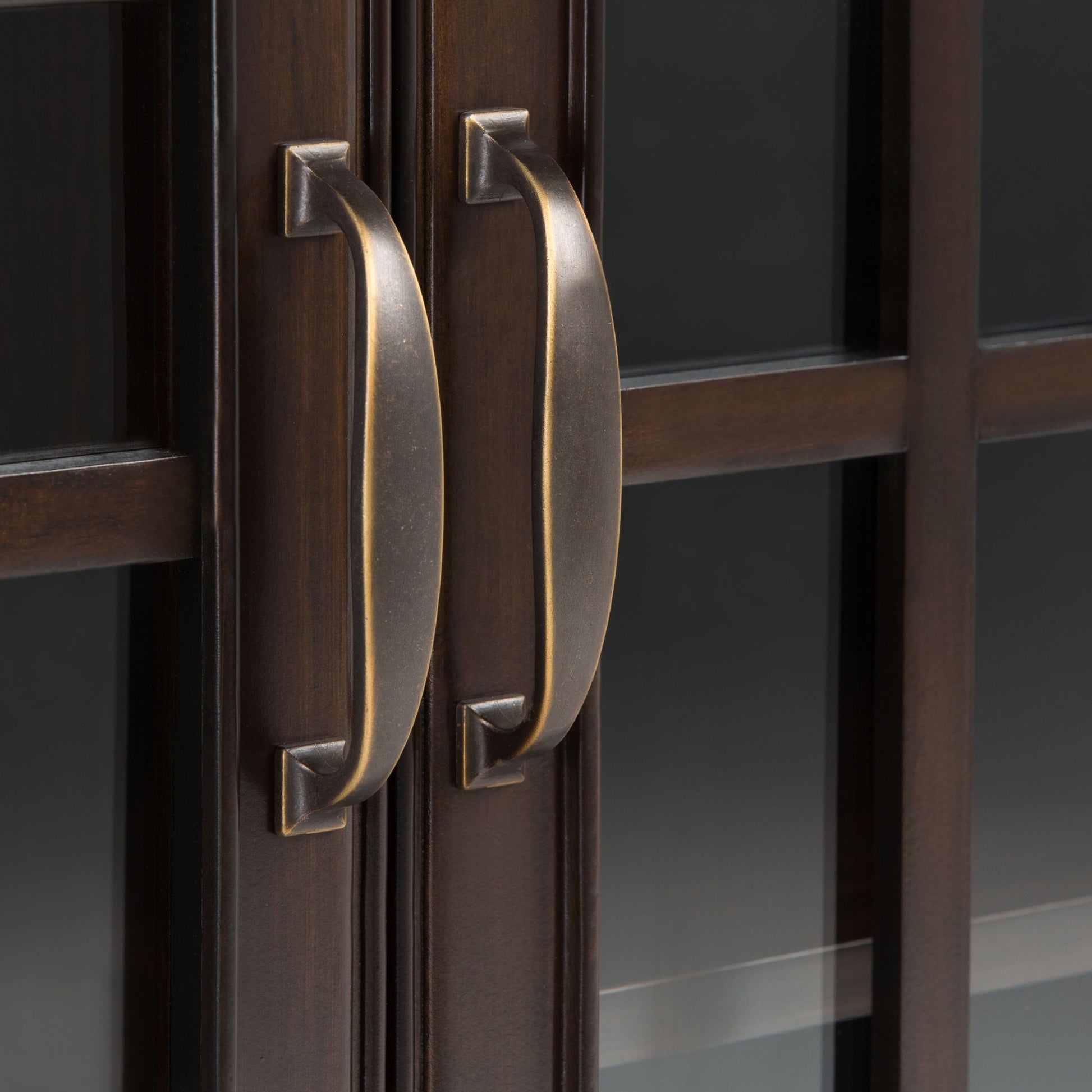 Close-up of two bronze handles on the dark wood doors of the Connaught - Handcrafted Low Storage Cabinet, highlighting reflections in the glass panels and details of the wood grain and metal finish.