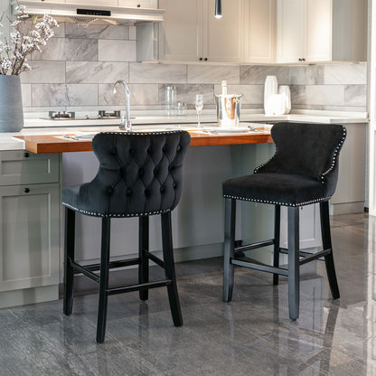 A set of two Contemporary Velvet Upholstered Wing-Back Barstools with button tufted backs, wooden legs, and chrome nailhead trim is placed at a kitchen island with a wood countertop in a modern kitchen with gray cabinets and a marble backsplash.