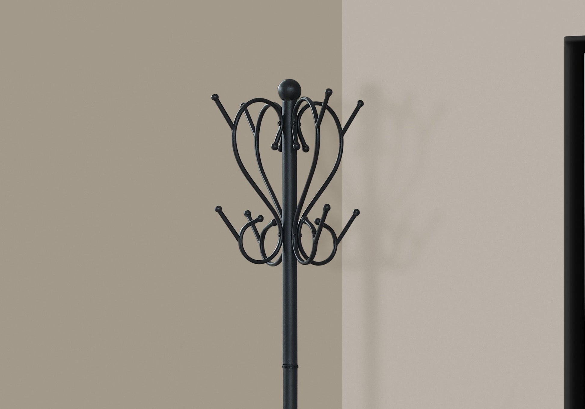 The Coat Rack, Hall Tree, Free Standing with 8 hooks and umbrella holder in transitional black stands against a beige wall, its shadow visible nearby and a dark rectangular doorway to the right.