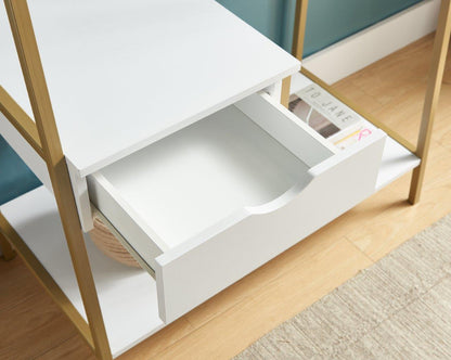 A white drawer is partially open in the Metal Clothes Rack Open Wardrobe Free Standing With One Drawer Hanging Clothes Rod, which has gold legs. A magazine and basket are on its shelves, placed on a light wood floor by a beige rug and blue wall.