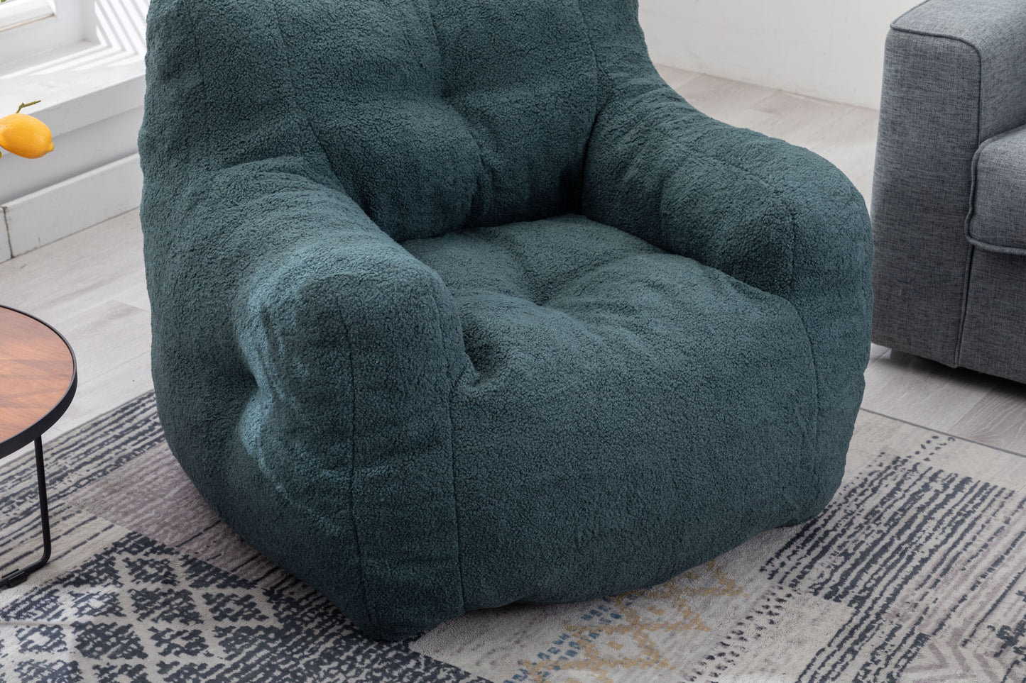 A Soft Teddy Fabric Tufted Foam Bean Bag Chair sits on a patterned rug near a gray sofa and a round wooden side table in a bright, modern living room.