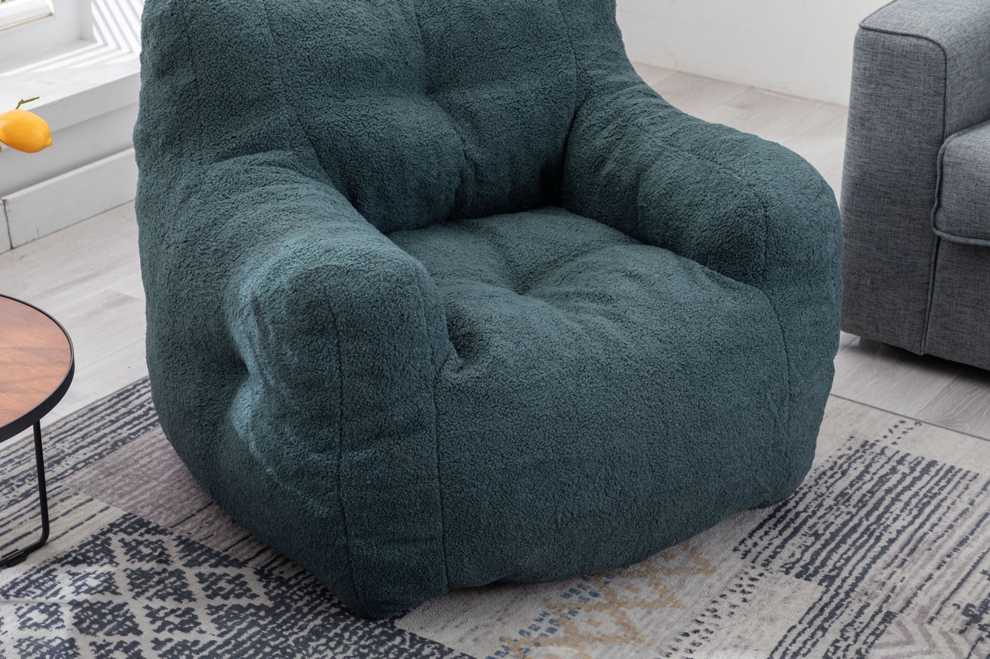 A Soft Teddy Fabric Tufted Foam Bean Bag Chair sits on a patterned rug near a gray sofa and a round wooden side table in a bright, modern living room.