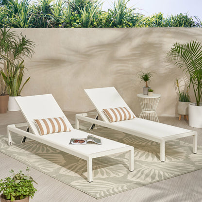 Two Outdoor Patio Chaise Lounges with 5 Reclining Positions, each with a striped pillow, sit on a leaf-patterned rug in a bright outdoor area with potted plants. An open magazine and sunglasses rest on one chaise near a light wall.