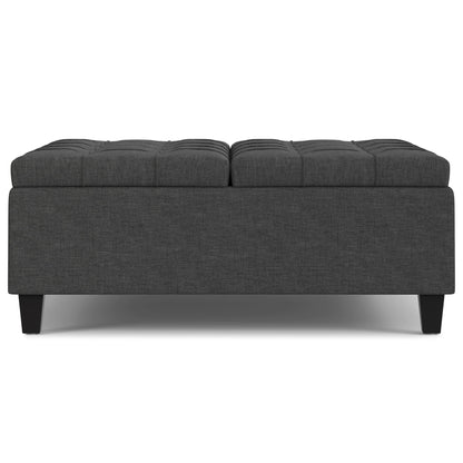 The Harrison Upholstered Coffee Table Storage Ottoman is rectangular, dark gray with tufted top cushioning, and features short black legs, shown from the front.
