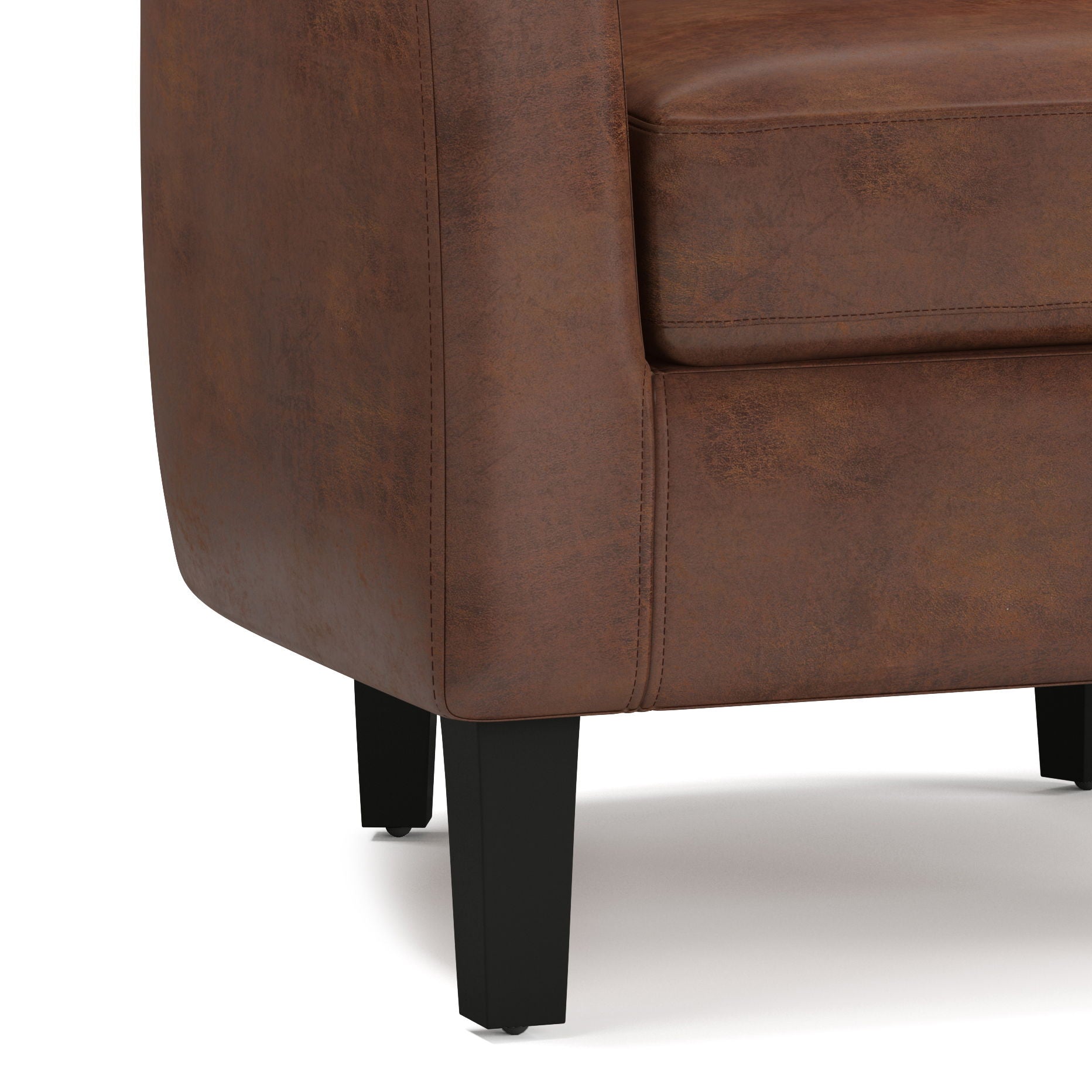 Close-up of the lower corner of the Austin - Handcrafted Tub Chair in brown leather, highlighting detailed stitching, part of the seat cushion, and two black wooden legs on a light surface.
