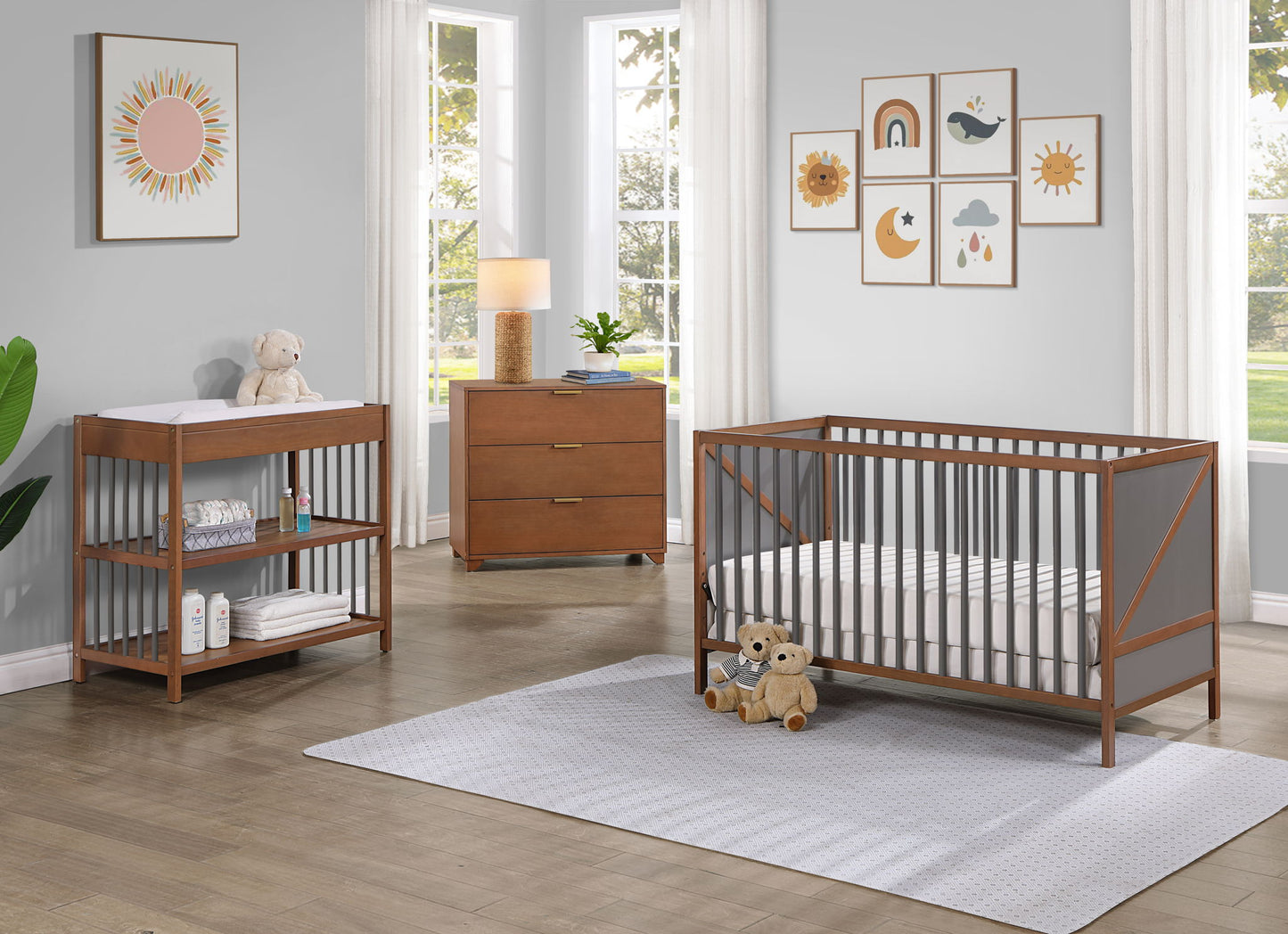 A modern nursery with the Pixie Zen 3-in-1 Crib in Walnut, a matching changing table with shelves, dresser, plush toys, wall art, lamp, and large windows with white curtains allowing natural light in.