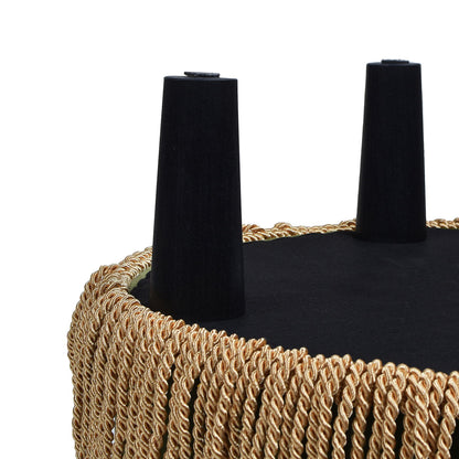 A close-up of the Yolanda Round Upholstered Accent Ottoman turned upside down, featuring two black angled legs and gold twisted rope fringe around the edge.
