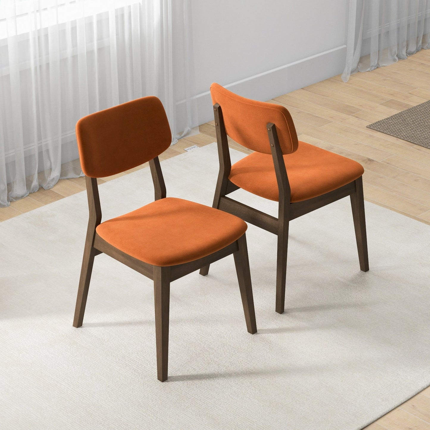 A set of two Carlos Solid Back Side Chairs with orange cushioned seats and dark wooden frames sit on a light rug in a bright room with wooden floors and sheer white curtains.