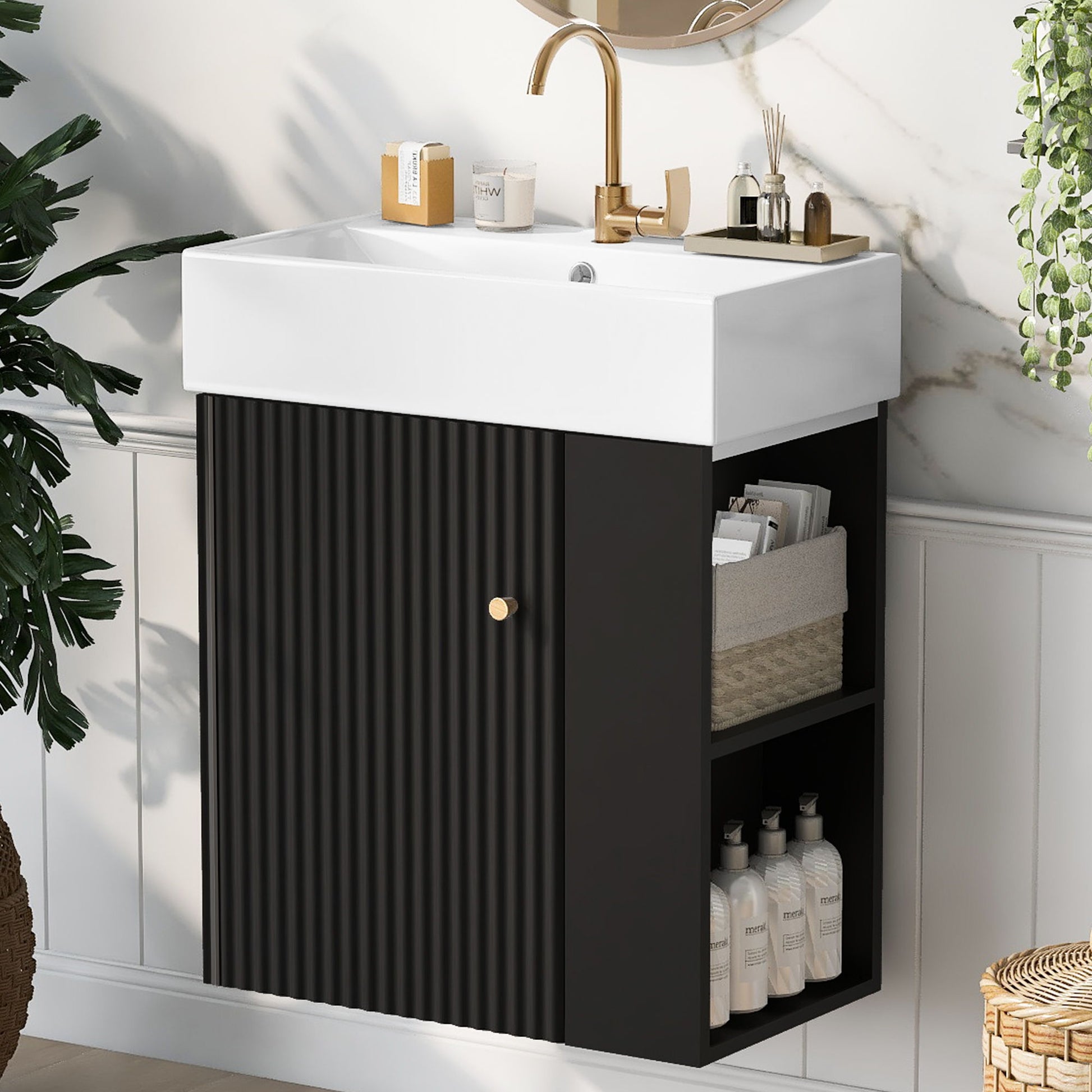 The Modern Floating Bathroom Vanity With Ceramic Basin, ideal for small bathrooms, features a gold faucet and black cabinet with vertical grooves. Open shelves display toiletries and a basket, while green plants enhance the decor.
