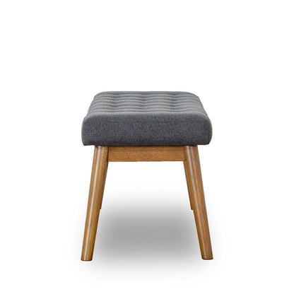 The Delilah Modern Bench features a cushioned, dark gray tufted seat and four angled wooden legs, displayed against a plain white background.