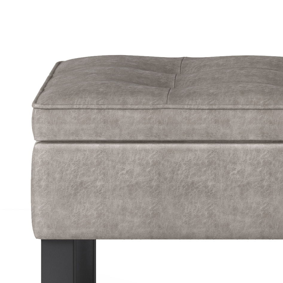 Close-up of the Cosmopolitan Storage Ottoman Bench With Open Bottom, upholstered in light gray faux leather with subtle tufted cushion and black rectangular legs.