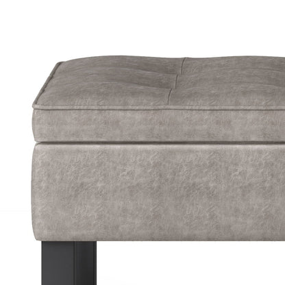Close-up of the Cosmopolitan Storage Ottoman Bench With Open Bottom, upholstered in light gray faux leather with subtle tufted cushion and black rectangular legs.