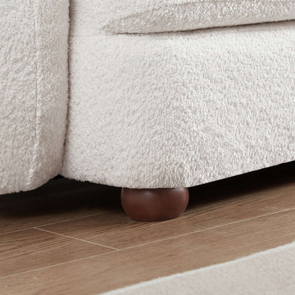 Close-up of the Paton - Comfortable Sofa in light beige with a textured finish and round wooden legs, shown on a wooden floor next to a light-colored rug.