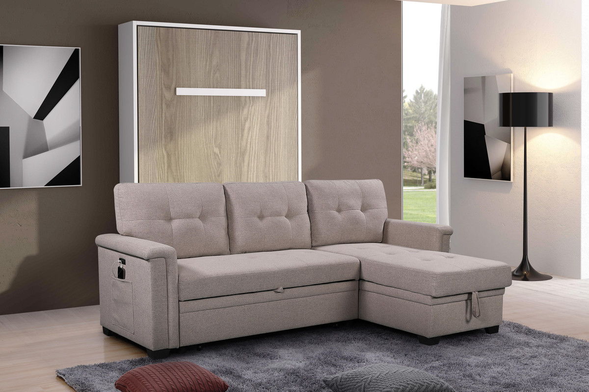 A modern living room with the Ashlyn Reversible Sleeper Sectional Sofa featuring storage, USB ports, and pocket, plus a wall-mounted wooden cabinet, abstract art, black floor lamp, gray textured rug on light wood floors, and large sunlit window.