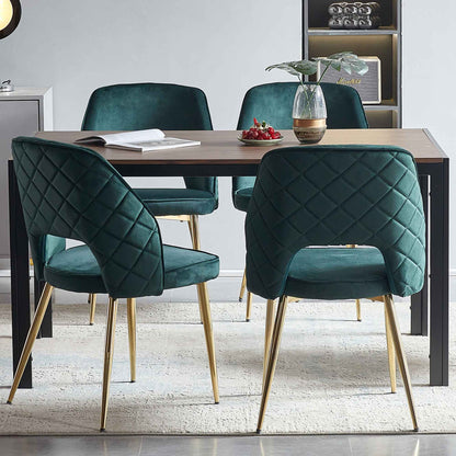 Four Velvet Dining Chairs With Metal Legs And Hollow Back surround a rectangular wooden table topped with an open book, small plant vase, and plate of red berries, all set on a light rug in a modern dining room.
