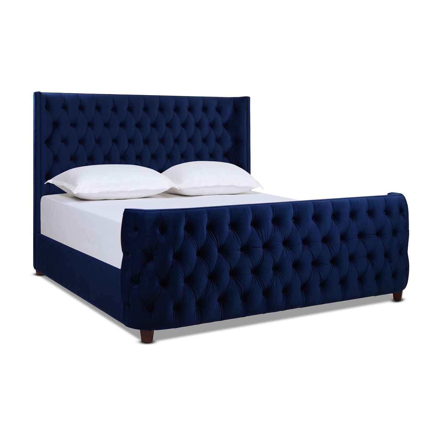 The Brooklyn Tufted Panel Bed features a navy blue upholstered headboard and footboard with deep button detailing. The set is shown with a white mattress and two white pillows.
