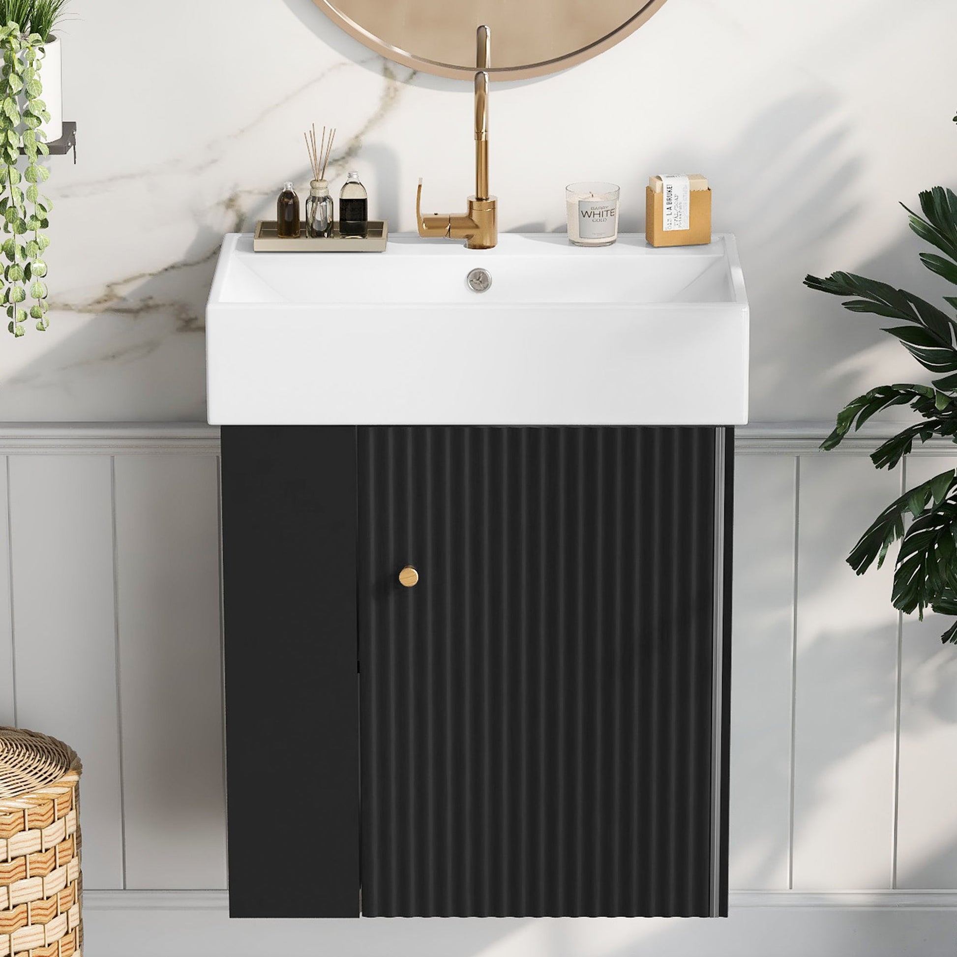 The Modern Floating Bathroom Vanity With Ceramic Basin, ideal for small bathrooms, features a gold faucet atop a black ribbed cabinet, complemented by a round mirror, decor accents, greenery, and stylish white paneled walls with marble highlights.