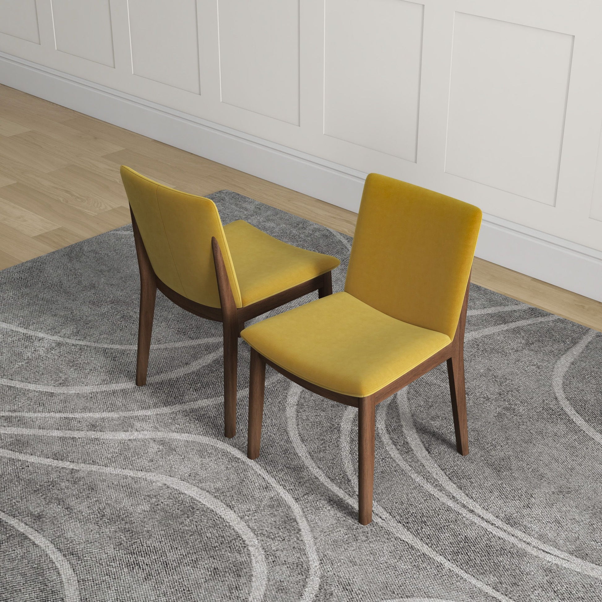 Two Laura Mid-Century Modern Solid Wood Dining Chairs (set of 2) with yellow upholstered seats and wooden legs sit on a gray patterned rug in a room with light wood floors and white paneled walls.