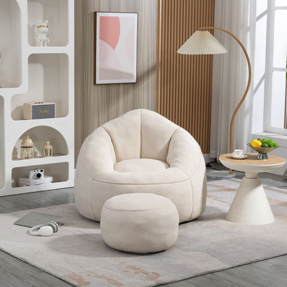 The Bedding Bean Bag Sofa Chair High Pressure Foam with Footrest sits on a light rug in a modern living room, next to a small round table with fruit, a lamp, shelves with decor, headphones, and a window with sheer curtains.