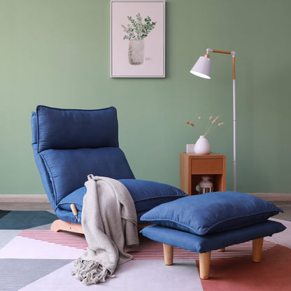 A Single Lazy Sofa Chair Leisure Foldable Reclining Chair in blue with a matching footrest sits on a geometric rug, draped with a gray blanket. A wooden side table and white floor lamp stand nearby against a green wall with framed plant art.