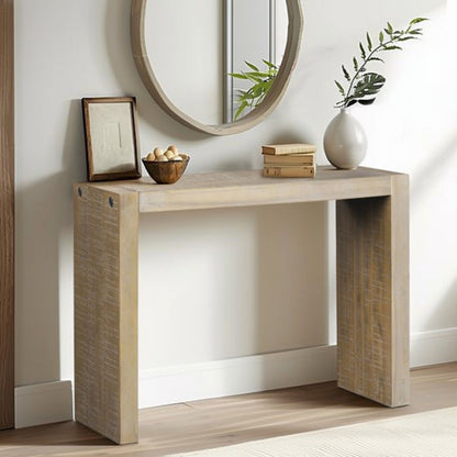 The Modern Design Console Table sits against a neutral wall with a round mirror, framed picture, bowl of nuts, vase of green branches, and two stacked books on top. Light wood flooring completes the scene.