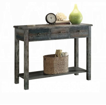 The Glancio - Console Table - Gray features three drawers, a lower shelf with a woven basket of rolled towels, and a top surface styled with a clock, books, decorative coral, and a green vase for a rustic touch.