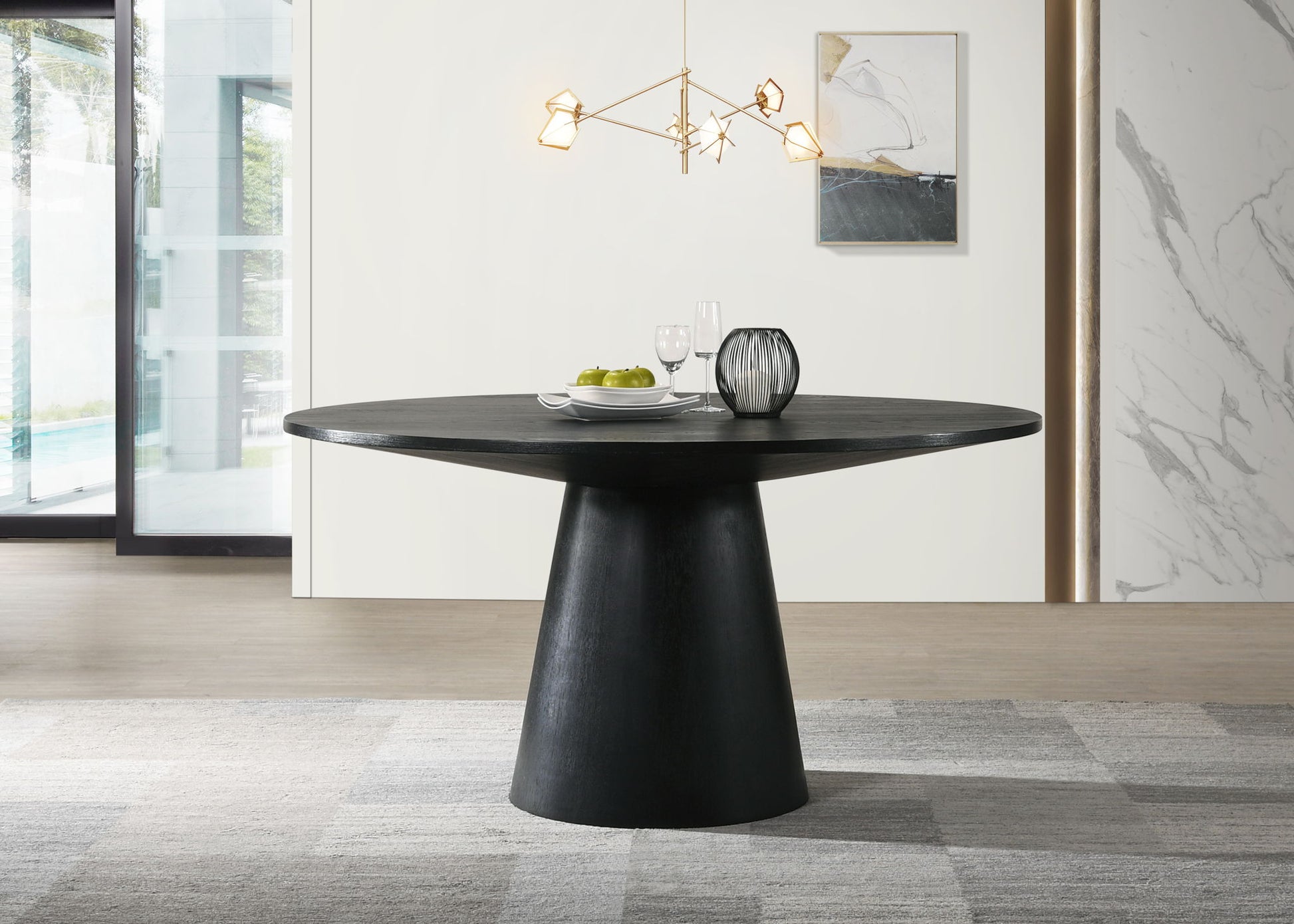 A modern dining room features the Jasper Wide Contemporary Round Dining Table in black, set with two glasses, a plate of green apples, and a decorative vase. Above hangs a geometric chandelier, with abstract wall art and large windows behind.