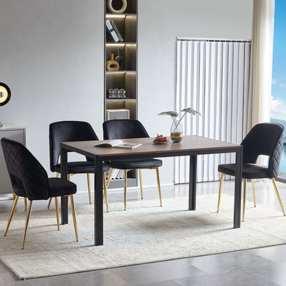 Modern dining room featuring a rectangular wooden table and four Velvet Dining Chairs With Metal Legs And Hollow Back, black with gold legs, plus a small plant, book on the table, and a built-in shelf with decor in the background.