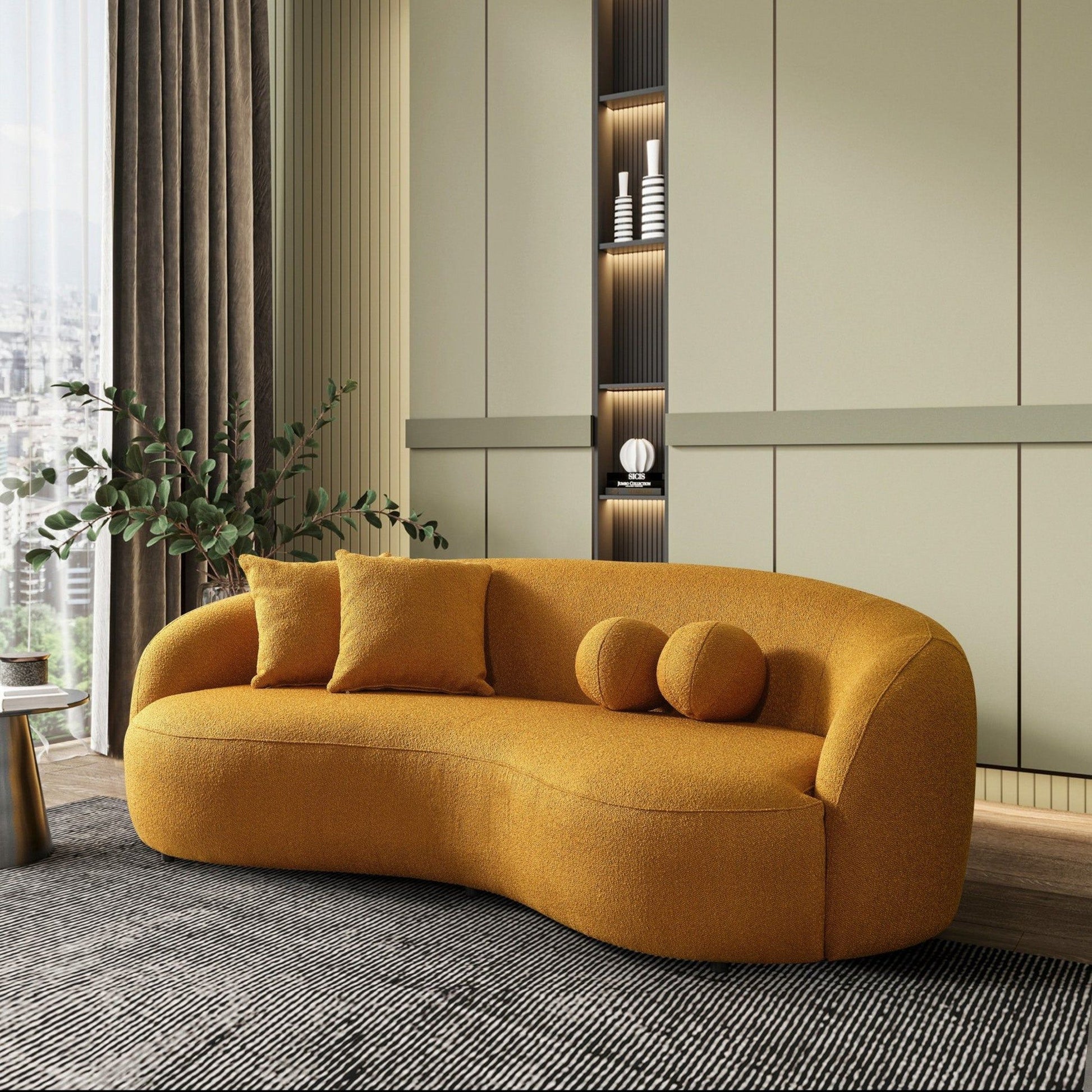 A modern living room showcases the Drake - Japandi Style Curvy Boucle Sofa in mustard yellow, three cushions, a large gray rug, leafy plant, and built-in shelves with décor against pale green paneled walls.
