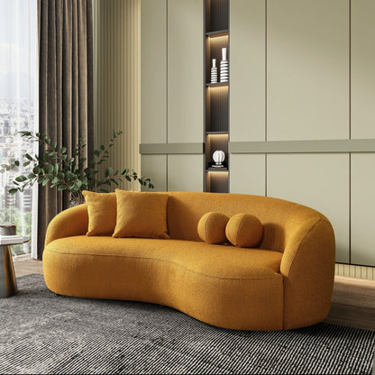 A modern living room showcases the Drake - Japandi Style Curvy Boucle Sofa in mustard yellow, three cushions, a large gray rug, leafy plant, and built-in shelves with décor against pale green paneled walls.
