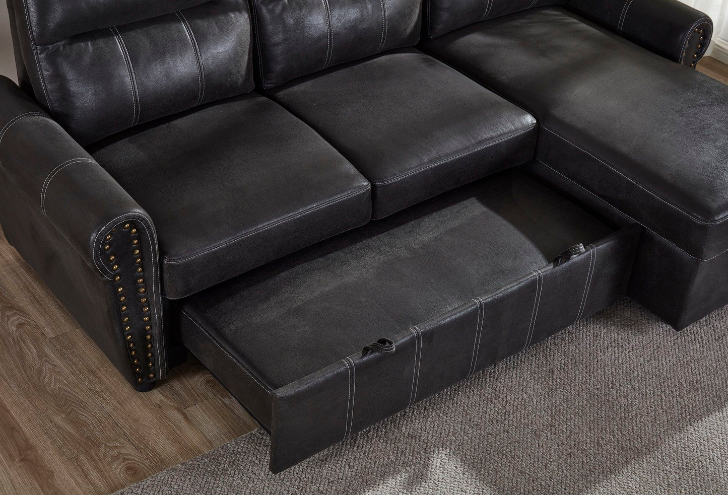 The Comfort Sectional Sofa Bed in black leather features an open pull-out storage drawer under the seat, and is shown on a wooden floor beside a light-colored textured rug.