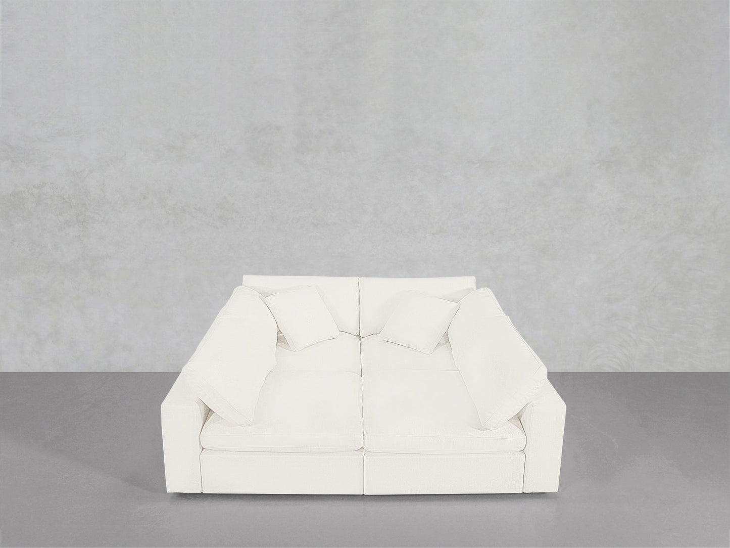A 4-Seat Modular Pit in white, paired with four matching cushions, sits against a light grey wall and floor in a minimalist, empty room.