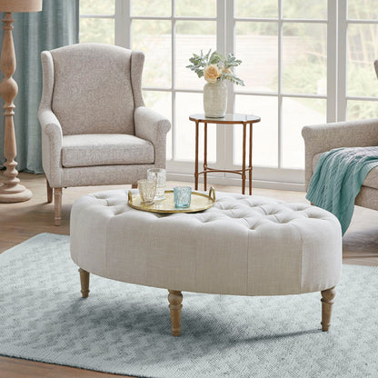 A cozy living room featuring the Fancy Style Design Upholstery Solid Wood - Linen armchair, a round ottoman, a serving tray with glassware, a side table with flowers, all on a light blue rug by large windows.