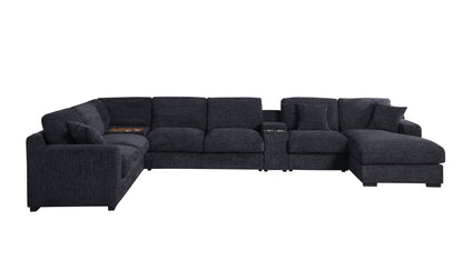 The large, dark gray Celine sectional is an L-shaped sofa in chenille fabric with plush cushions and a right-facing chaise. It includes built-in cup holders, charging ports, and a small storage compartment on the left section.