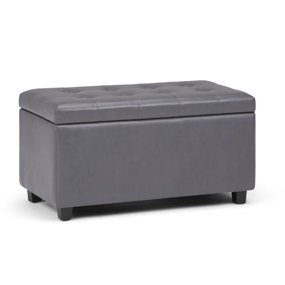 The Cosmopolitan Upholstered Storage Ottoman is rectangular, features a tufted dark gray faux leather design with short black legs, and has a hinged top that lifts for convenient storage inside.