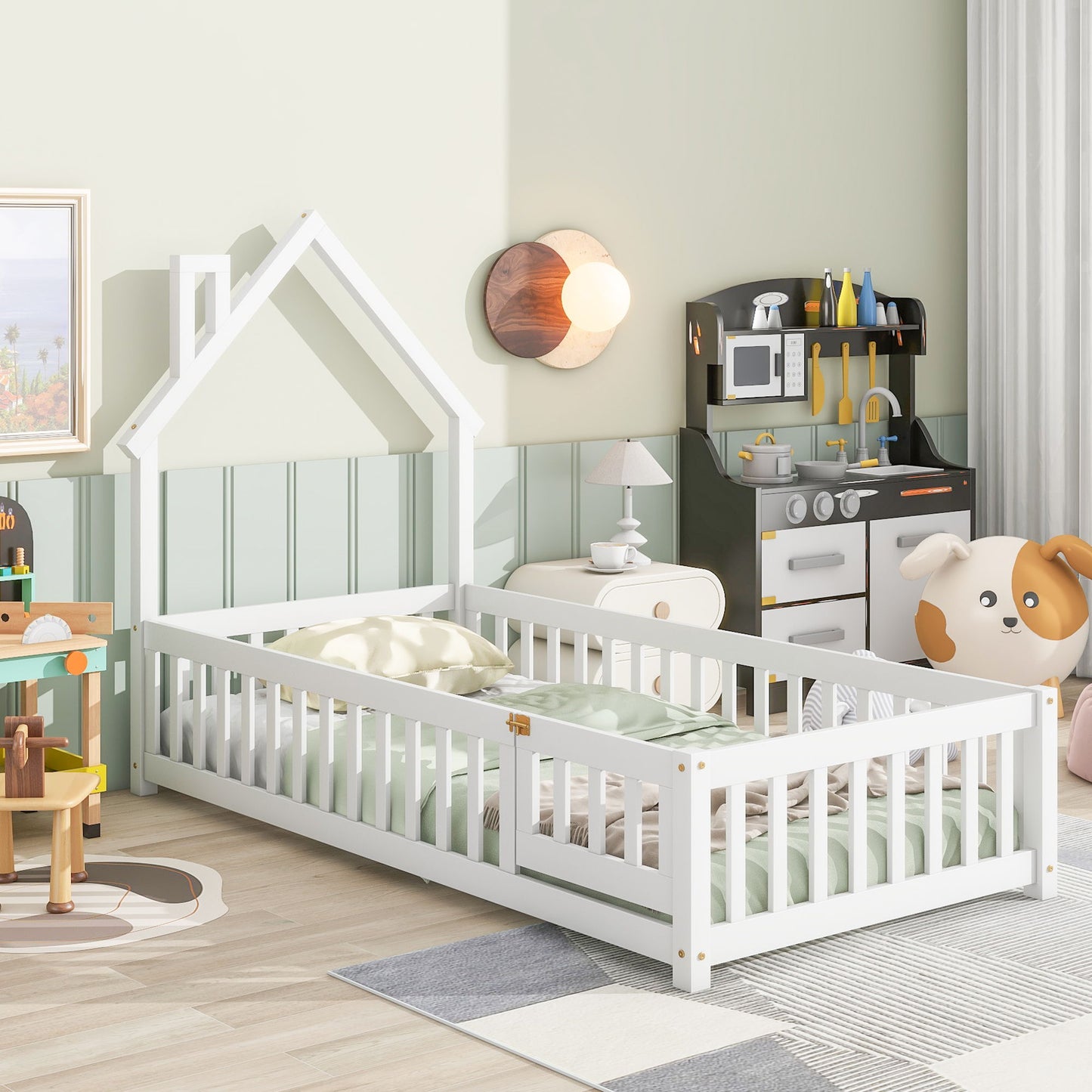 A cozy children’s bedroom features the House-Shaped Headboard Floor Bed With Fence, pastel bedding, a toy kitchen set, a plush dog chair, and playful decor on light green walls. Sunlight brightens the tidy, colorful space.