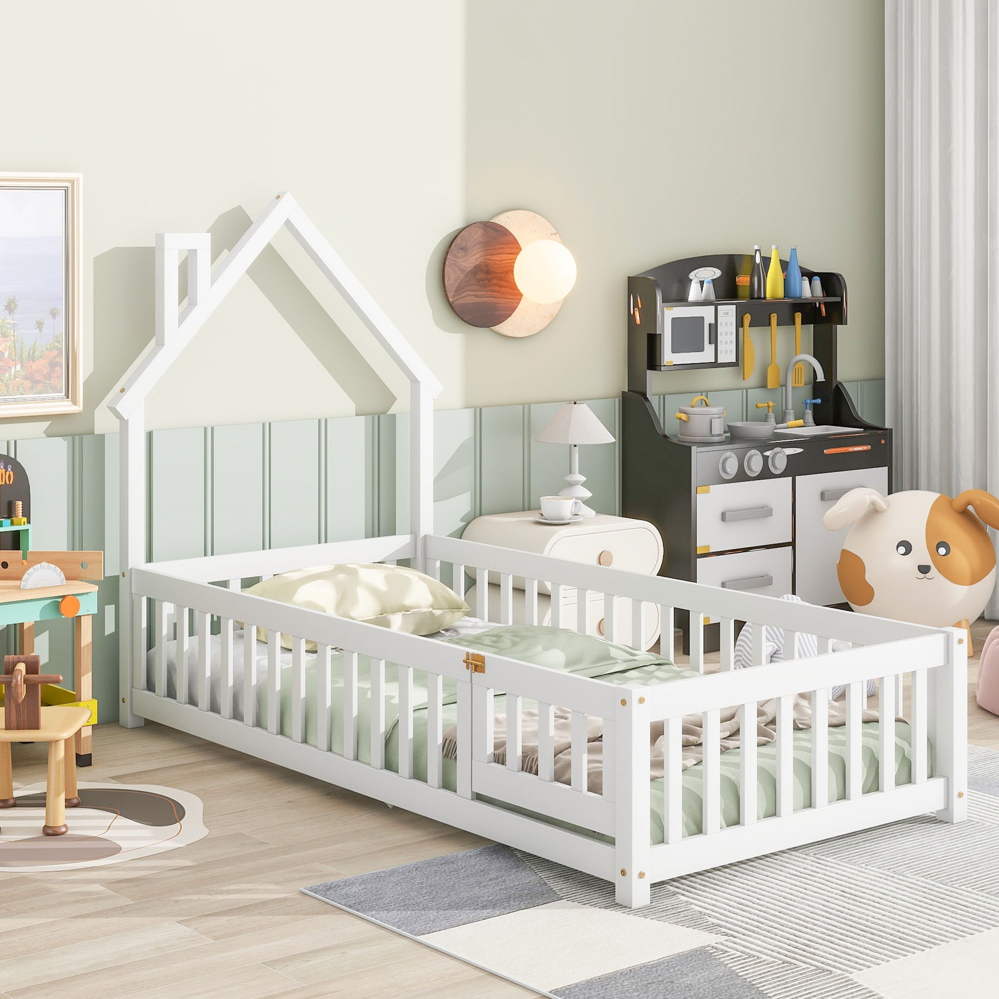 A cozy children’s bedroom features the House-Shaped Headboard Floor Bed With Fence, pastel bedding, a toy kitchen set, a plush dog chair, and playful decor on light green walls. Sunlight brightens the tidy, colorful space.