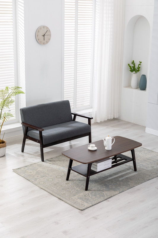 A modern living room featuring the Bahamas - Living Room Set, including a gray loveseat, dark wood coffee table, light patterned rug, potted plant, decorative vases on a shelf, wall clock, and large windows with white blinds and sheer curtains.