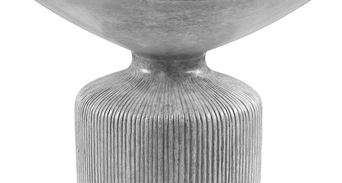 A close-up of the Laddie - Weathered Table, featuring a modern, metallic gray design with a rounded top and a textured, vertically ribbed cylindrical base against a white background.