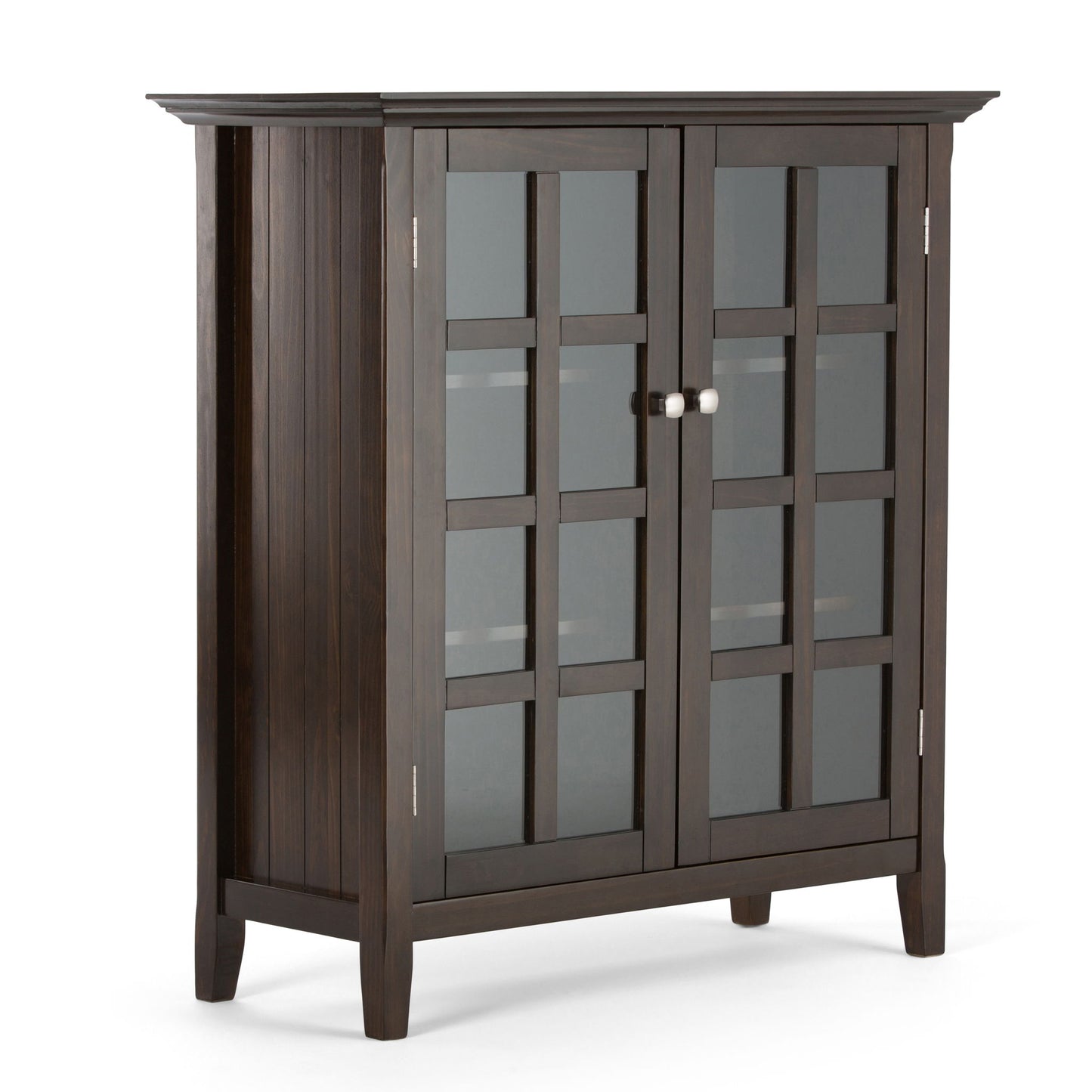 The Acadian - Medium Storage Cabinet is handcrafted from dark wood, featuring two grid-patterned glass doors with metal knobs, four sturdy legs, and a slightly overhanging top.